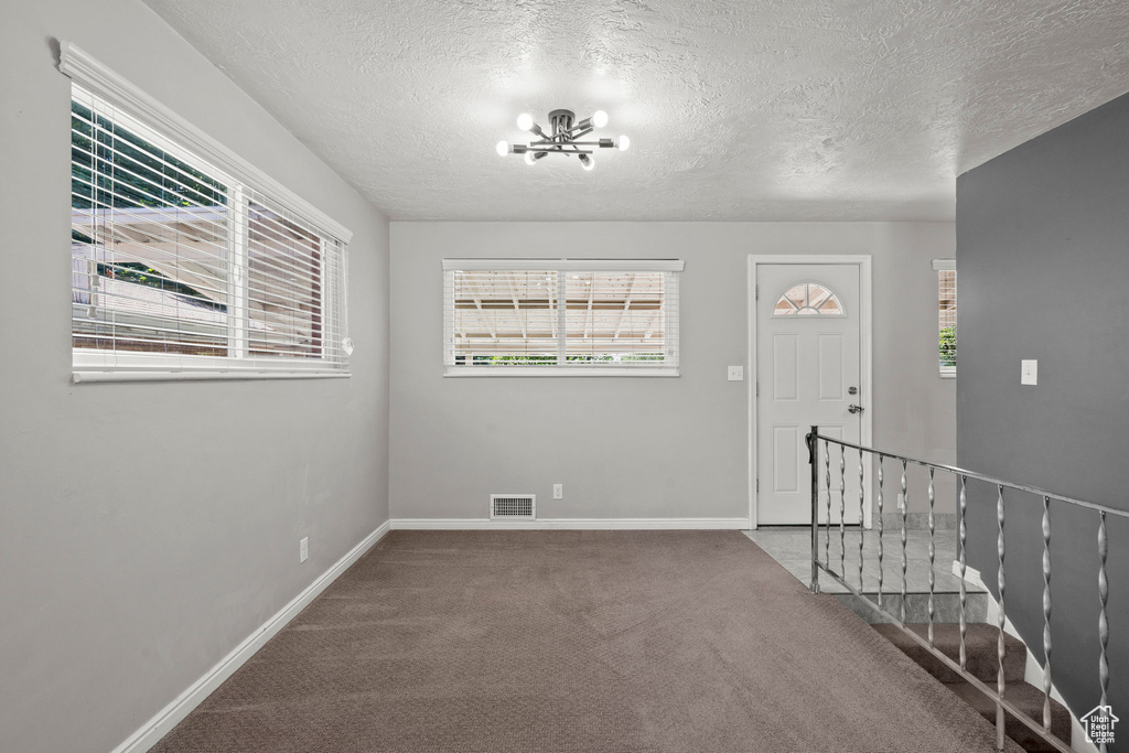 Carpeted entrance foyer featuring a chandelier, baseboards, and a textured ceiling