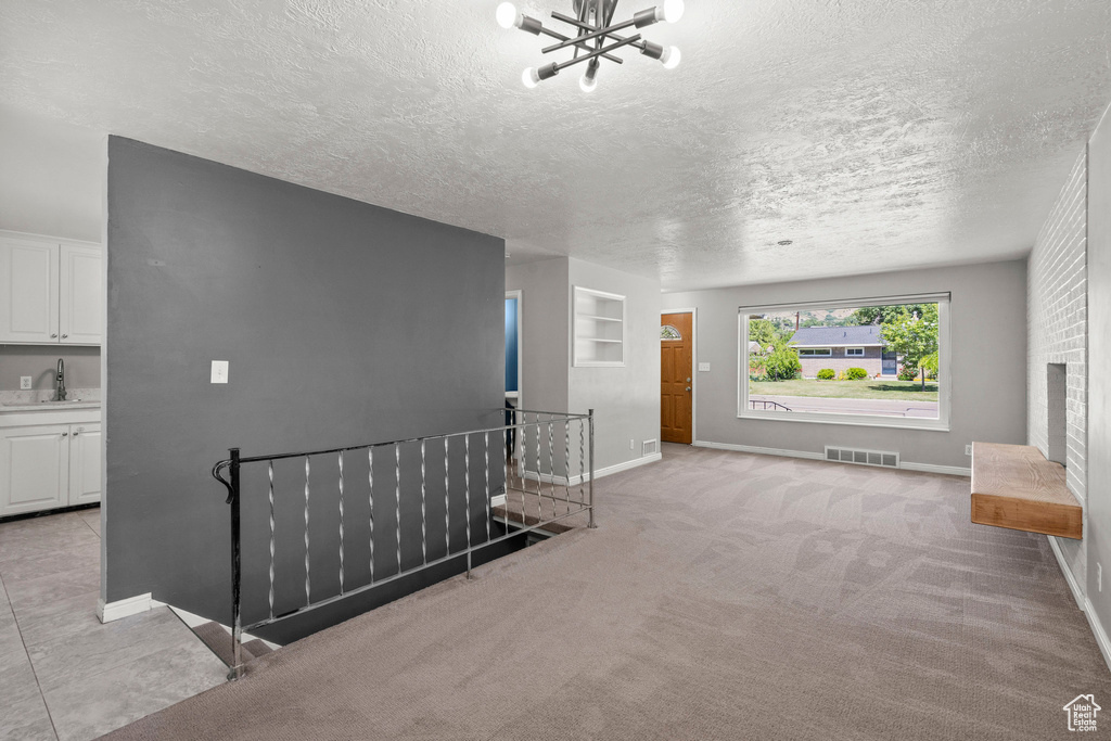 Unfurnished living room with a sink, a chandelier, a textured ceiling, baseboards, and a fireplace