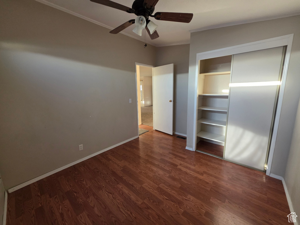 Unfurnished bedroom featuring ornamental molding, dark wood finished floors, baseboards, and ceiling fan