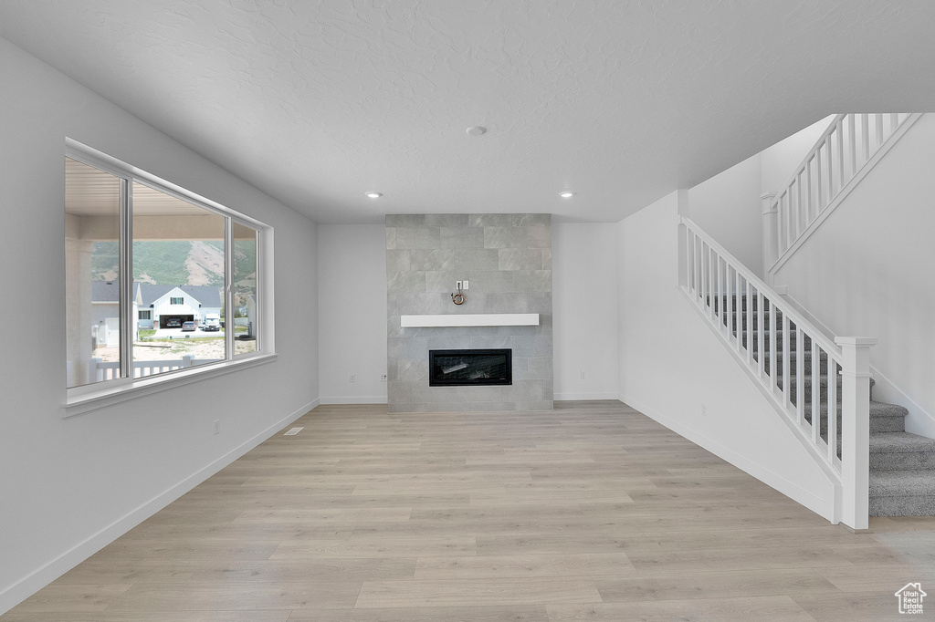 Unfurnished living room featuring stairway, a fireplace, light wood finished floors, recessed lighting, and baseboards