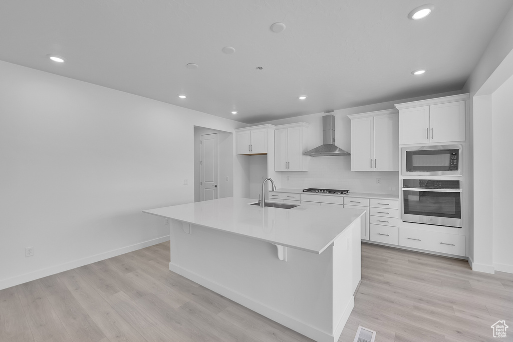 Kitchen with wall chimney exhaust hood, stainless steel oven, a sink, built in microwave, and an island with sink