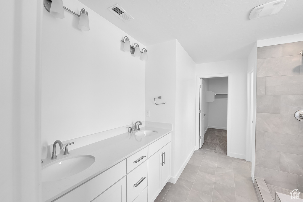 Full bath with tiled shower, double vanity, a walk in closet, baseboards, and marble finish floors