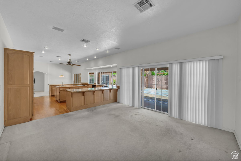Kitchen with ceiling fan, a kitchen breakfast bar, light colored carpet, a sink, and recessed lighting