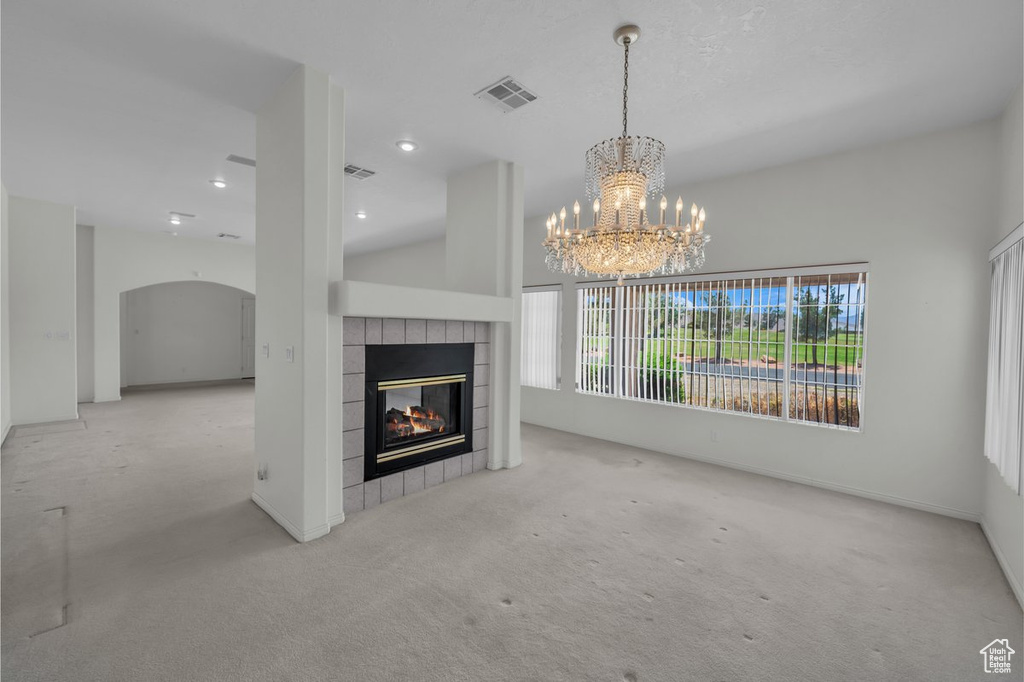 Unfurnished living room featuring a tile fireplace, a chandelier, carpet floors, arched walkways, and recessed lighting