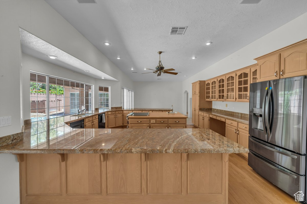 Kitchen featuring stainless steel refrigerator with ice dispenser, a sink, a peninsula, a breakfast bar area, and glass insert cabinets