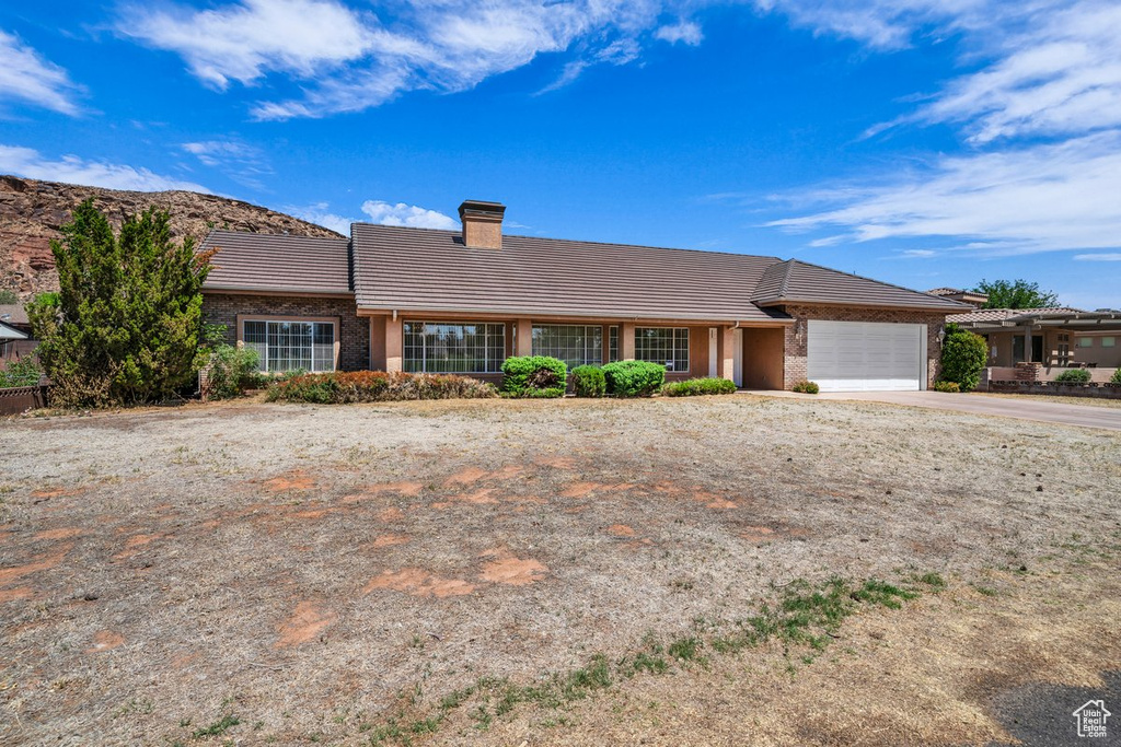 Single story home featuring a tile roof, an attached garage, a chimney, and driveway