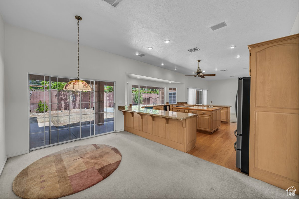 Kitchen featuring freestanding refrigerator, recessed lighting, ceiling fan, a kitchen breakfast bar, and light stone counters