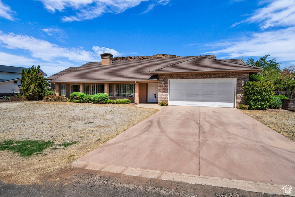Single story home featuring a tile roof, an attached garage, concrete driveway, a chimney, and brick siding