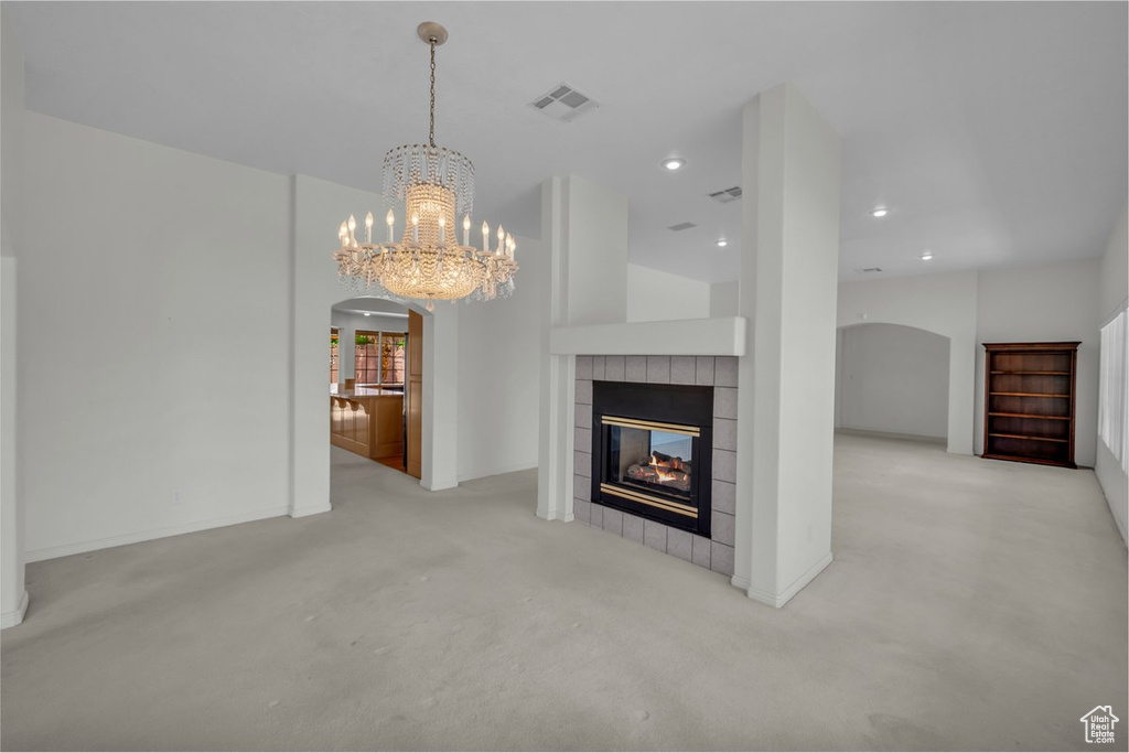 Unfurnished living room featuring arched walkways, a chandelier, a tile fireplace, carpet flooring, and recessed lighting