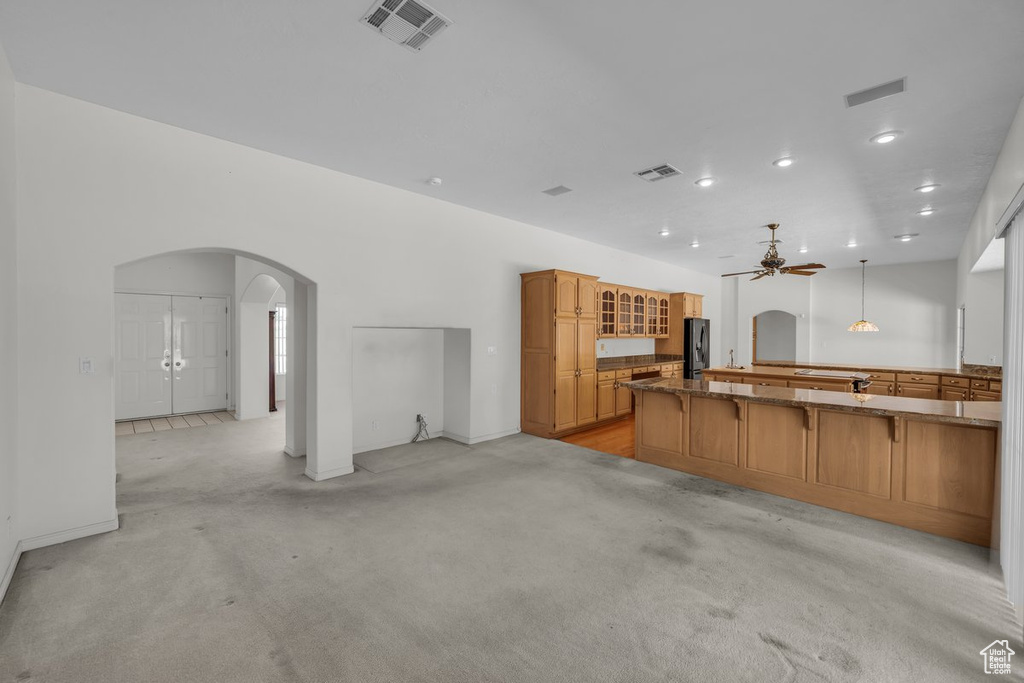 Kitchen with arched walkways, fridge with ice dispenser, a ceiling fan, a kitchen breakfast bar, and brown cabinets