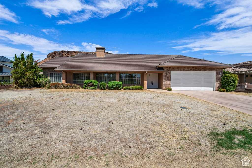 Ranch-style house with a tile roof, an attached garage, concrete driveway, and a chimney