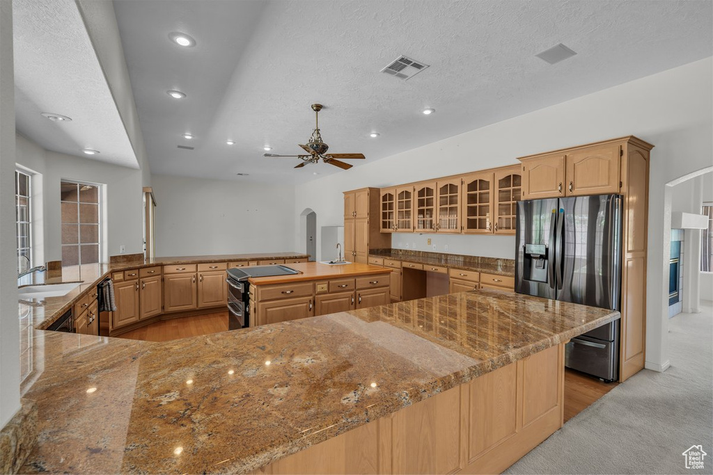 Kitchen with black fridge with ice dispenser, a sink, arched walkways, a ceiling fan, and a center island with sink