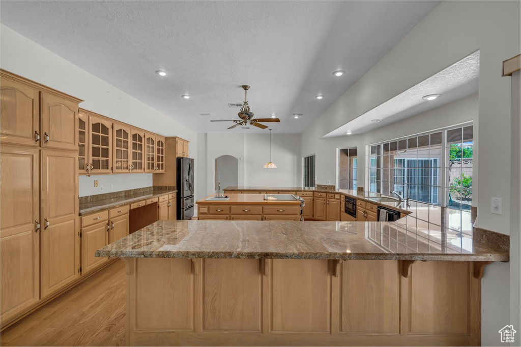 Kitchen with stainless steel fridge with ice dispenser, a kitchen breakfast bar, recessed lighting, light wood-type flooring, and a sink