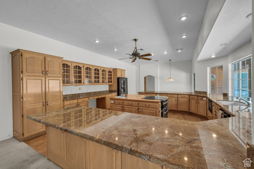 Kitchen featuring black refrigerator with ice dispenser, a large island, recessed lighting, arched walkways, and a sink