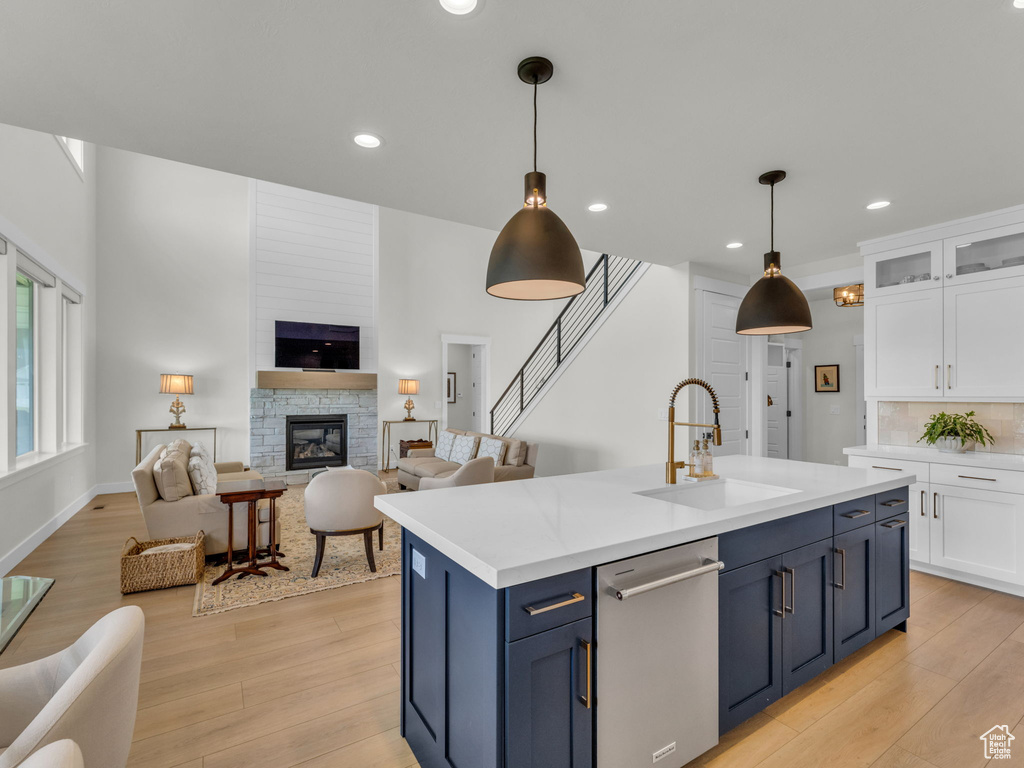 Kitchen with dishwasher, a sink, white cabinetry, open floor plan, and light wood finished floors