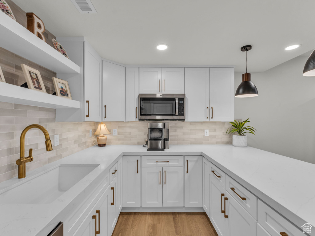 Kitchen featuring stainless steel microwave, open shelves, a sink, white cabinets, and decorative backsplash