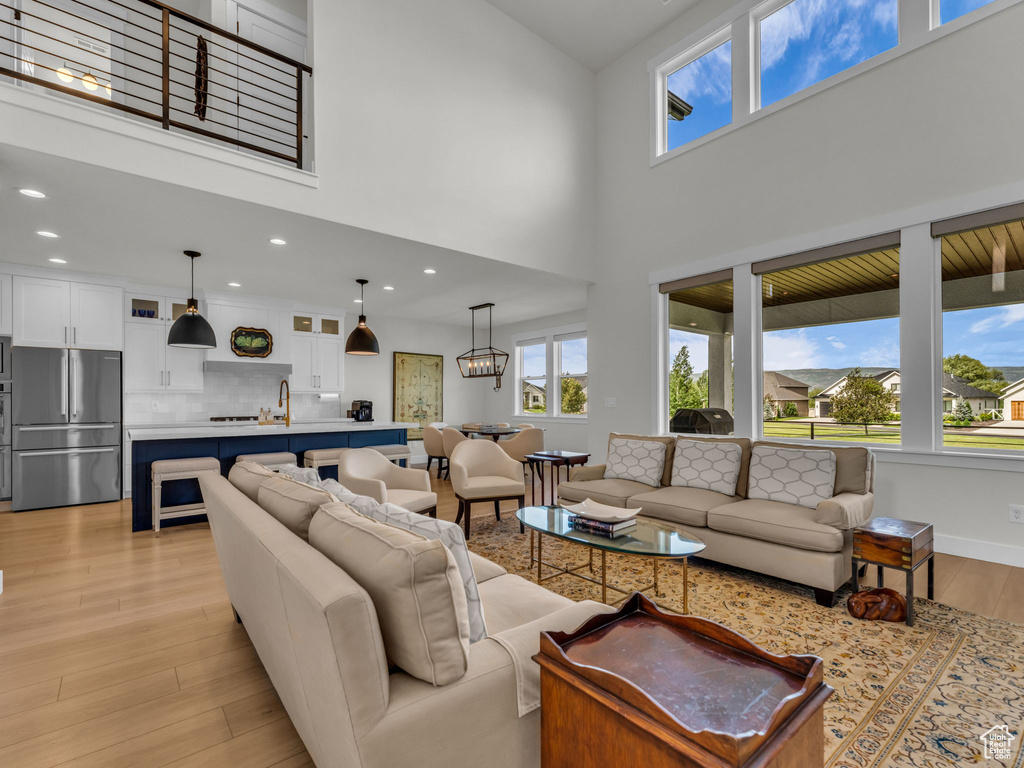 Living room with light wood finished floors, a towering ceiling, and recessed lighting