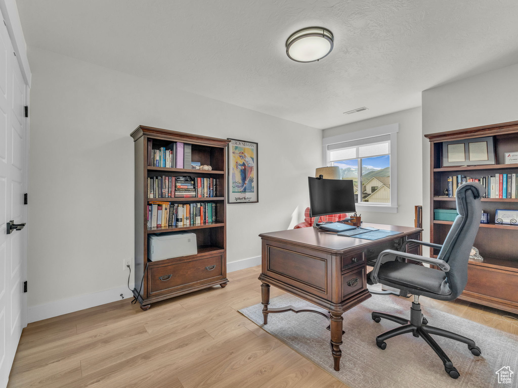 Office area featuring light wood-type flooring, baseboards, and a textured ceiling