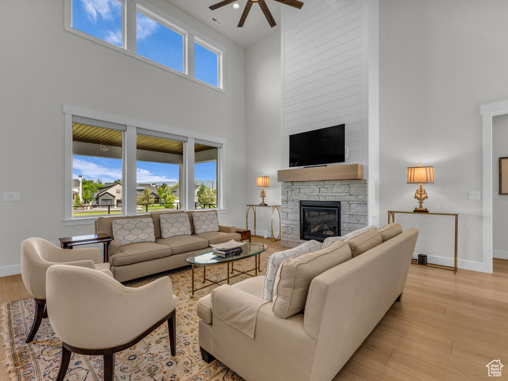 Living room with a high ceiling, a ceiling fan, a fireplace, baseboards, and light wood-type flooring