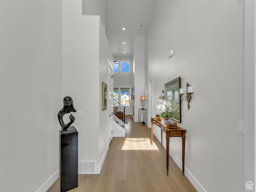 Corridor featuring light wood-style floors, recessed lighting, baseboards, and a high ceiling