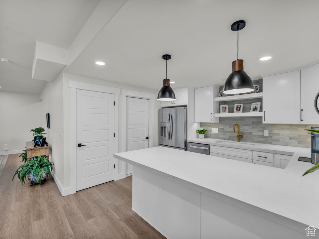 Kitchen featuring stainless steel appliances, a sink, light countertops, open shelves, and white cabinetry