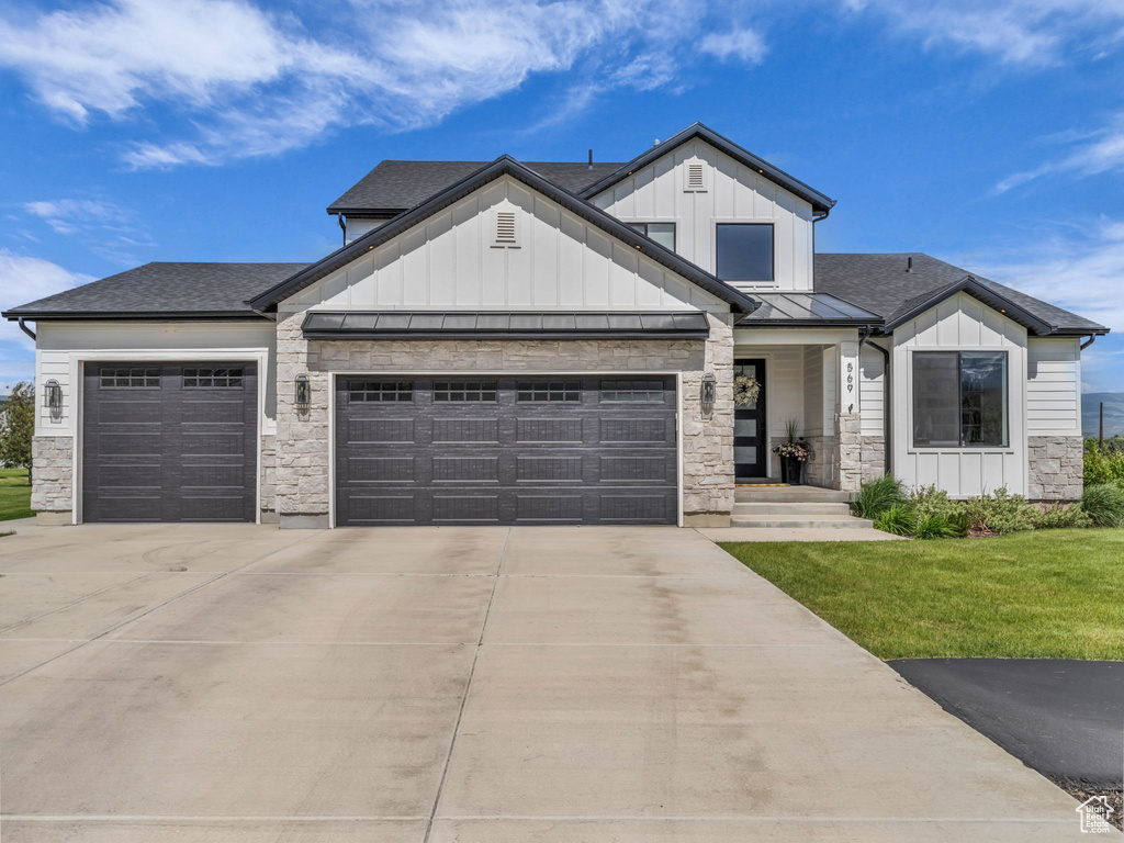 Modern farmhouse with a garage, driveway, board and batten siding, a standing seam roof, and stone siding