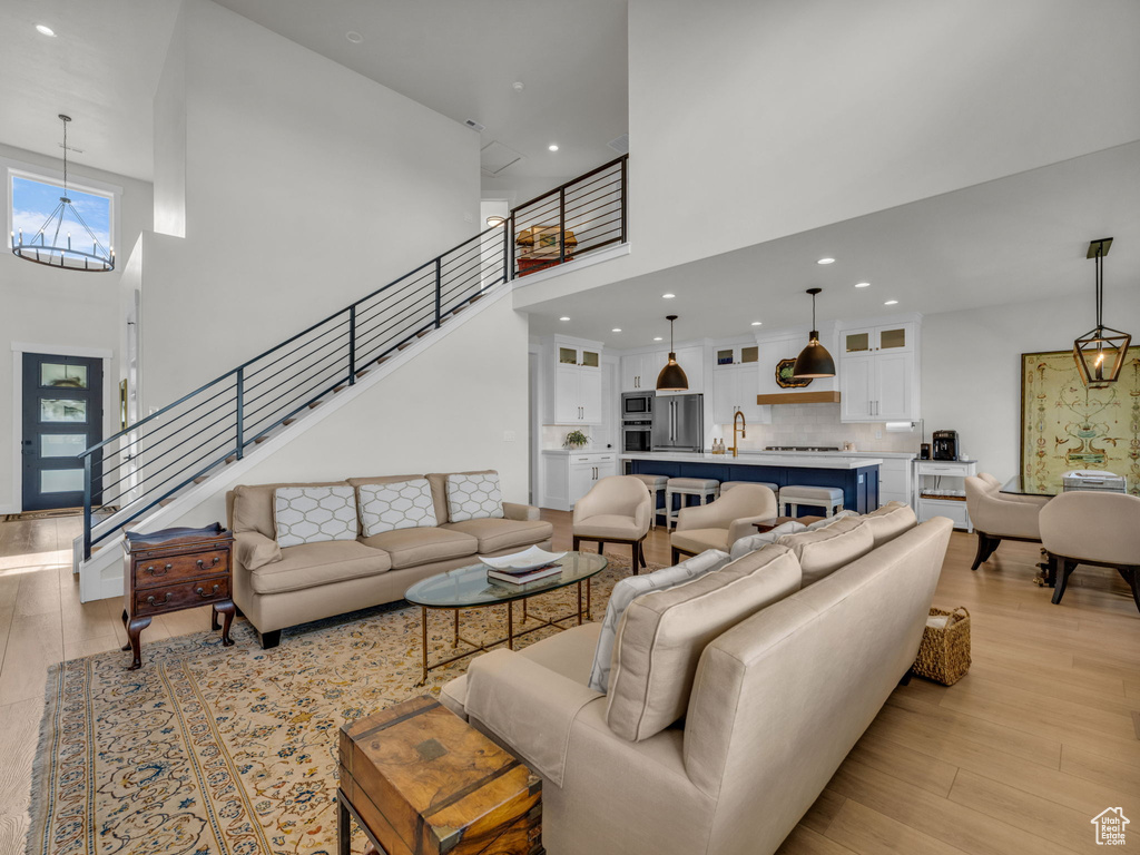 Living room with a towering ceiling, light wood-style floors, a chandelier, recessed lighting, and stairway