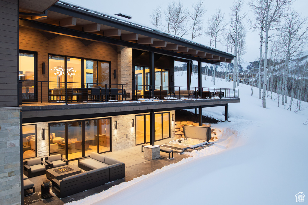 Snow covered house featuring an outdoor living space with a fire pit, stone siding, and a patio area