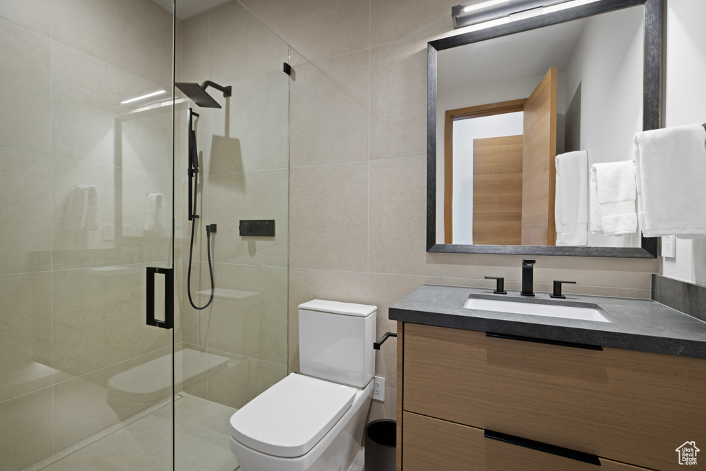 Bathroom featuring toilet, a stall shower, tile walls, and vanity