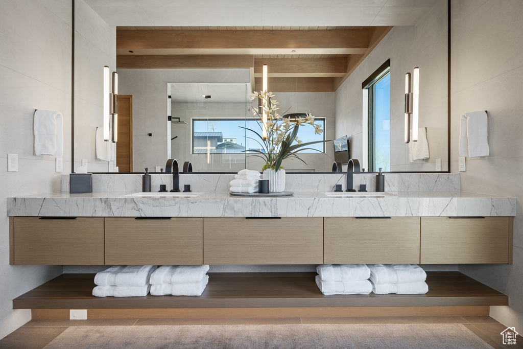 Full bathroom featuring double vanity, beamed ceiling, and healthy amount of natural light