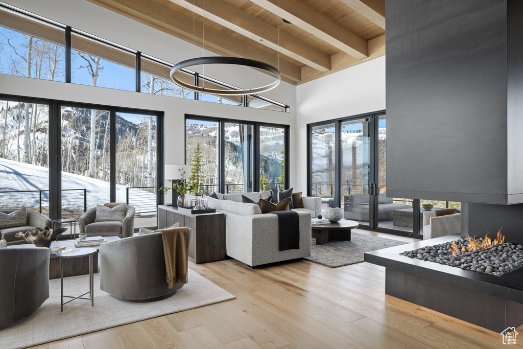 Living area with wooden ceiling with exposed beams, wood finished floors, plenty of natural light, a towering ceiling, and french doors