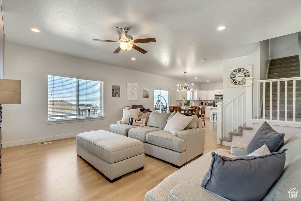 Living room featuring stairs, ceiling fan, a chandelier, recessed lighting, and light wood-style floors
