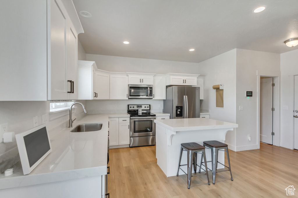 Kitchen featuring appliances with stainless steel finishes, a sink, a kitchen breakfast bar, a kitchen island, and white cabinets
