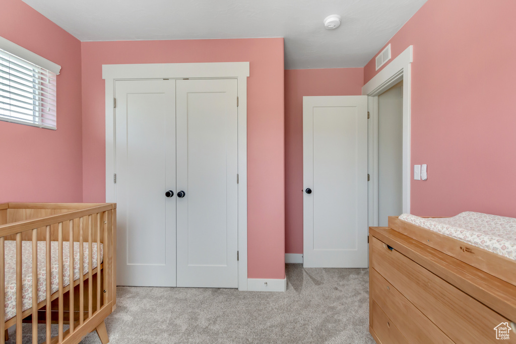 Bedroom with a closet, light carpet, a crib, and baseboards