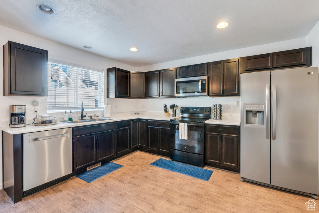 Kitchen with stainless steel appliances, a sink, light countertops, light wood-style flooring, and recessed lighting