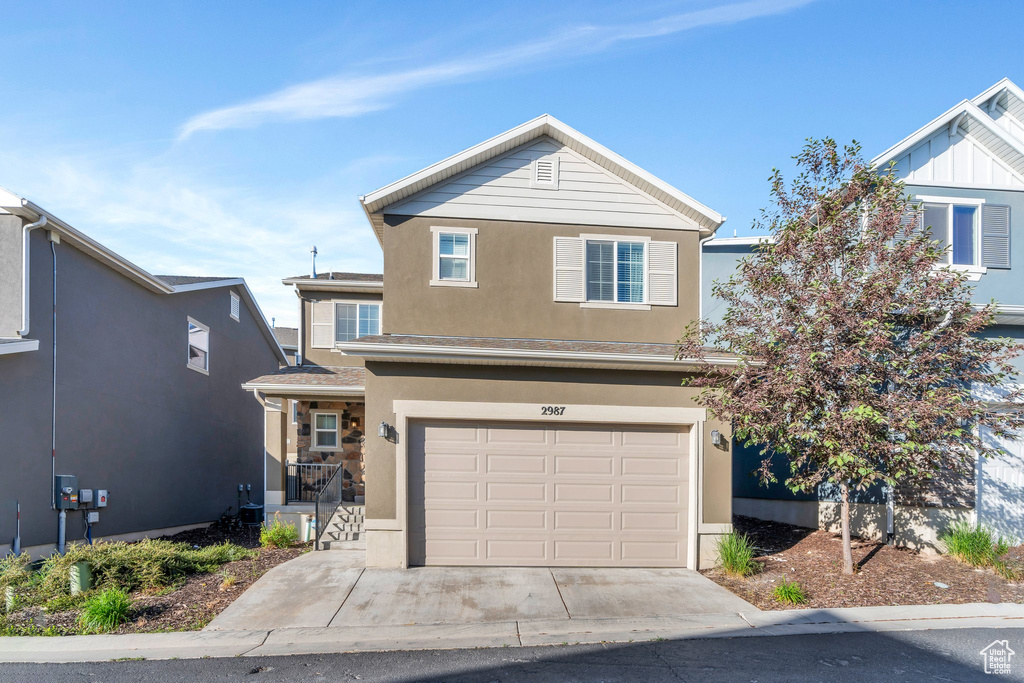 Traditional home with stucco siding, an attached garage, and driveway