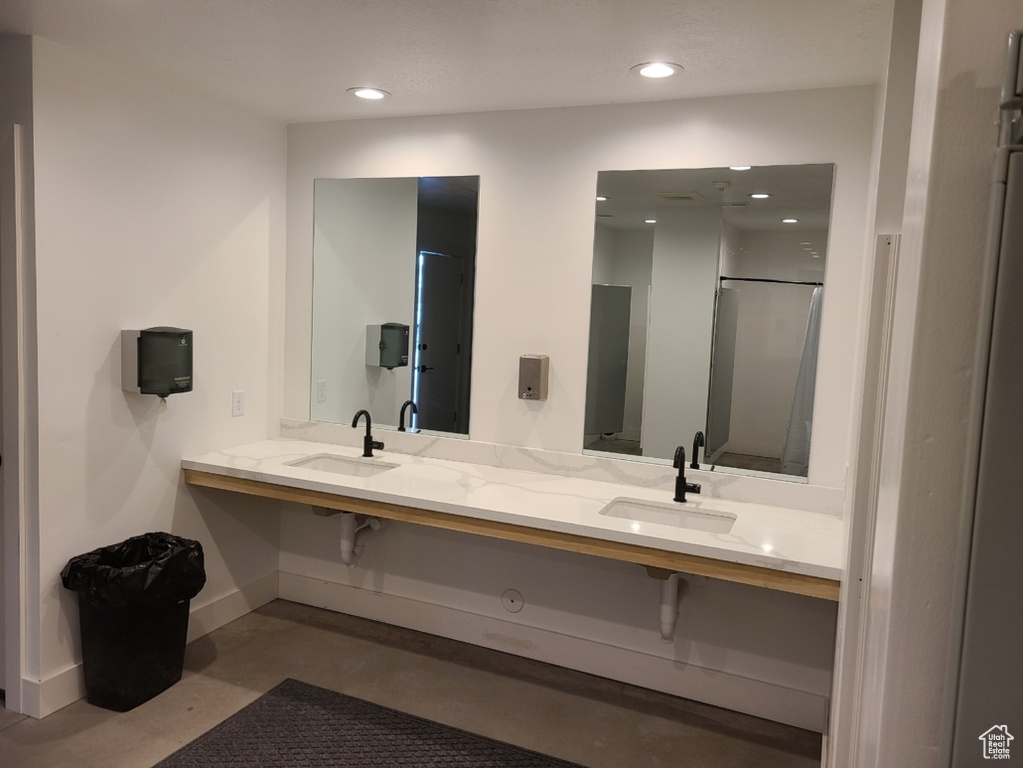 Bathroom with baseboards, recessed lighting, finished concrete floors, double vanity, and a shower with shower door