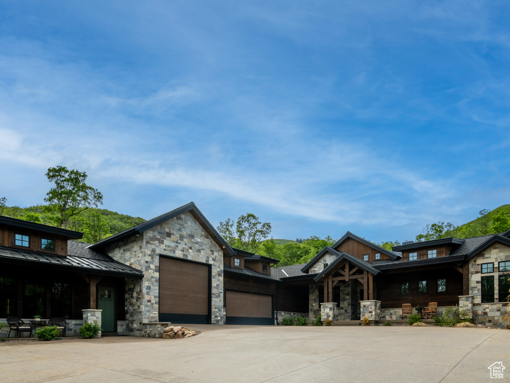 View of front of home featuring stone siding, a standing seam roof, a garage, covered porch, and driveway