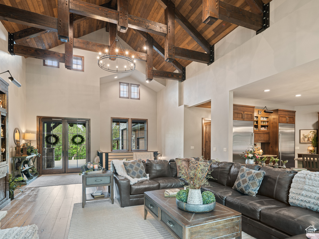 Living room with high vaulted ceiling, wooden ceiling with exposed beams, light wood-style flooring, a chandelier, and french doors