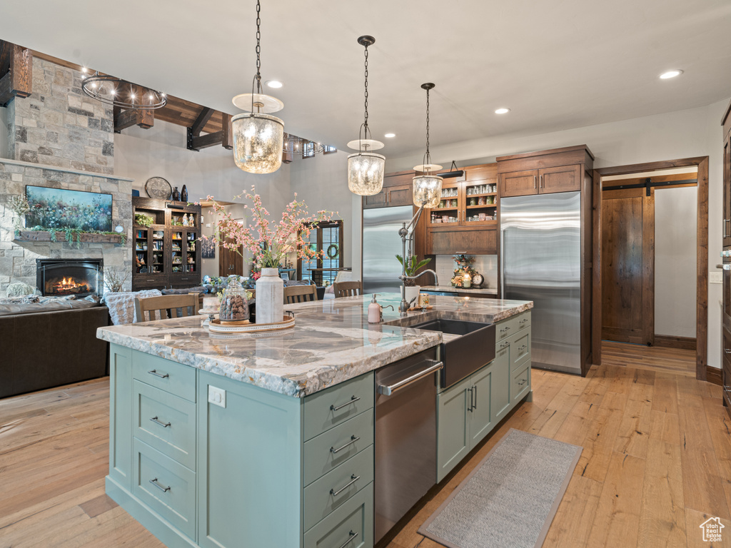 Kitchen with appliances with stainless steel finishes, a sink, light wood-type flooring, light stone countertops, and hanging light fixtures