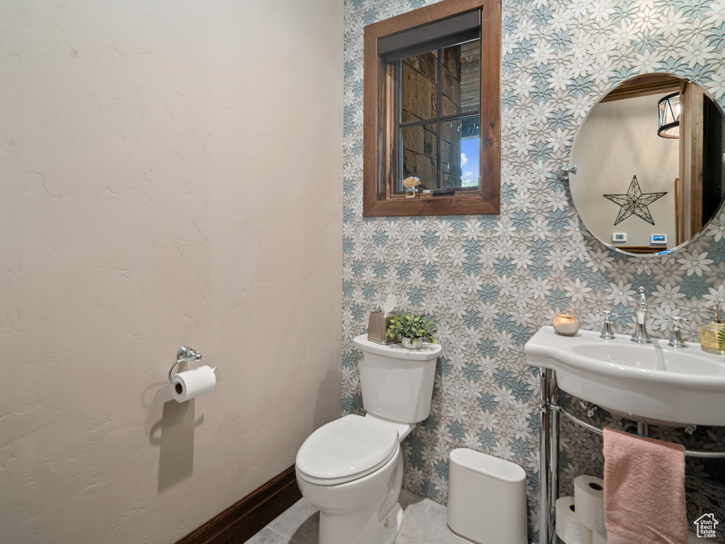 Half bathroom with toilet, a sink, and wallpapered walls