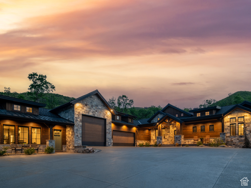 Contemporary house with stone siding, a standing seam roof, a garage, driveway, and metal roof
