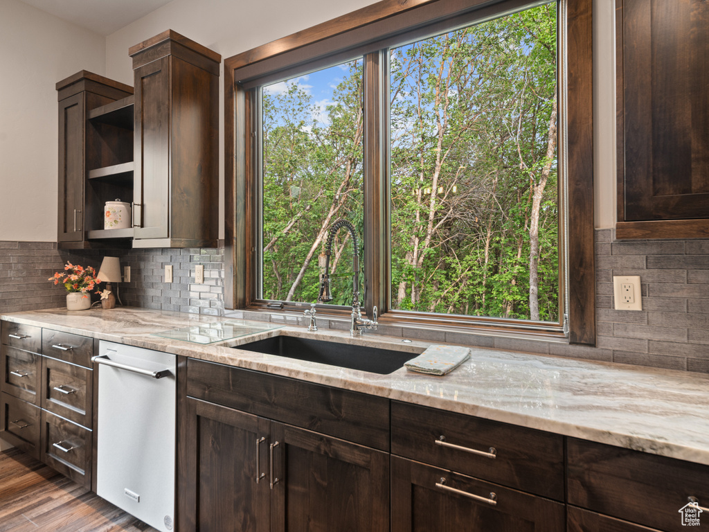 Kitchen with a sink, dark brown cabinets, open shelves, light stone countertops, and decorative backsplash