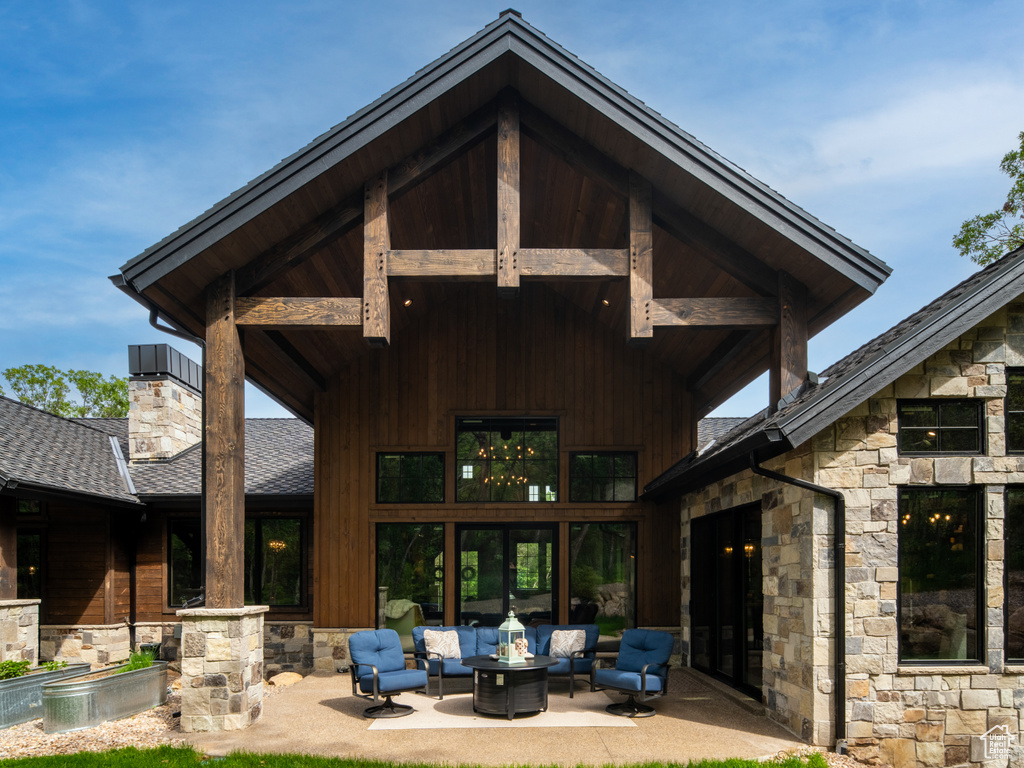 Back of house featuring an outdoor living space with a fire pit, stone siding, a patio, and a shingled roof