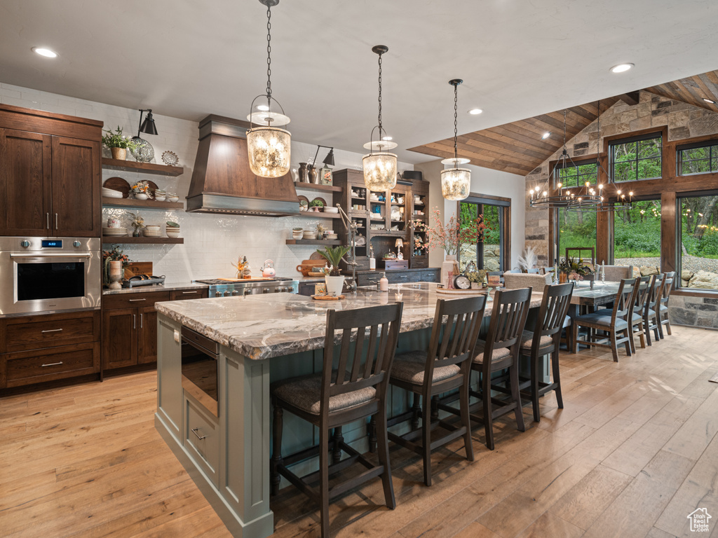 Kitchen with open shelves, oven, custom range hood, a chandelier, and light stone countertops