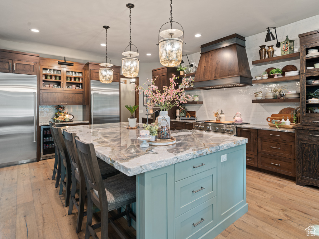 Kitchen with stainless steel appliances, premium range hood, open shelves, wine cooler, and decorative backsplash