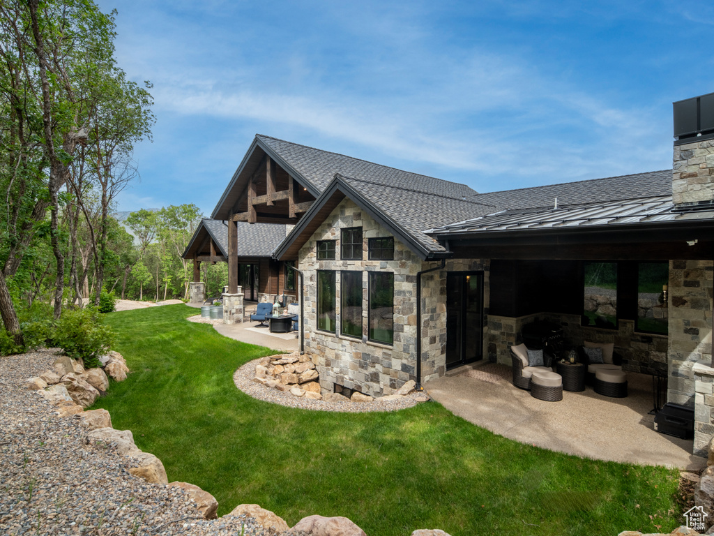 Back of property with stone siding, a patio area, a lawn, a standing seam roof, and roof with shingles