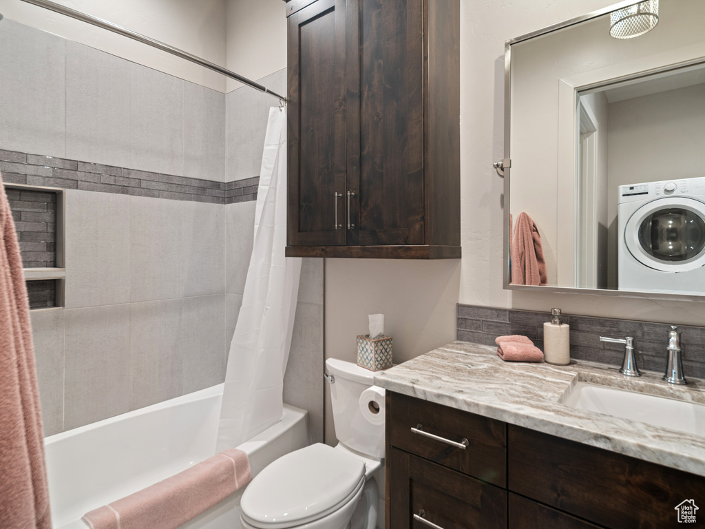 Bathroom with washer / dryer, vanity, shower / bath combination with curtain, and toilet
