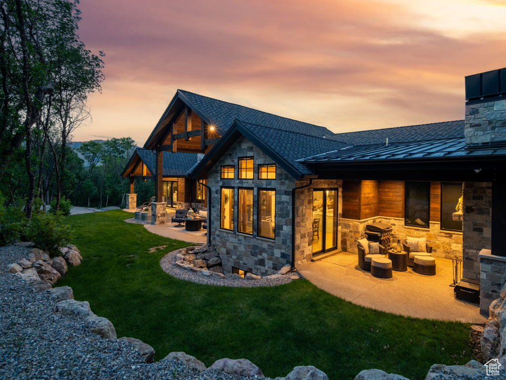 Back of property at dusk featuring a standing seam roof, stone siding, a patio, and an outdoor living space