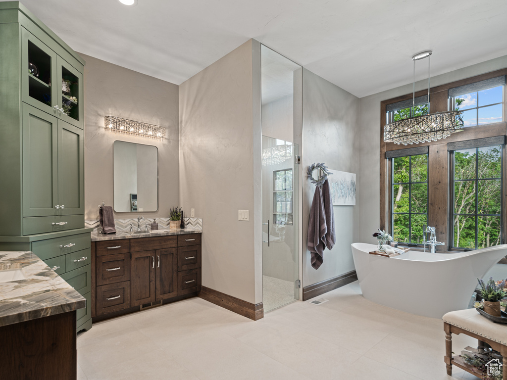 Full bathroom with vanity, a soaking tub, a stall shower, a chandelier, and baseboards